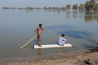 Zwei Männer auf einem Floss auf einem überschwemmten Feld in Pakistan 2022.
