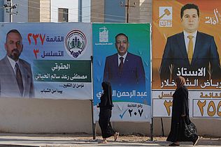 Frauen laufen vor Wahlplakaten mit den Bildern von Männern.