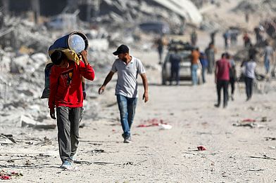 Ein Junge läuft bepackt durch Trümmer in Gaza.