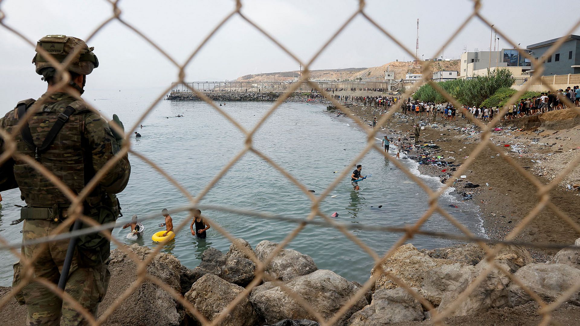 Ein Angehöriger des spanischen Militärs hält an einem Zaun Wache, während Menschen durch das Wasser waten und versuchen, nach Spanien zu gelangen. Ceuta, Spanien, 31.07.2026. REUTERS/Jon Nazca
